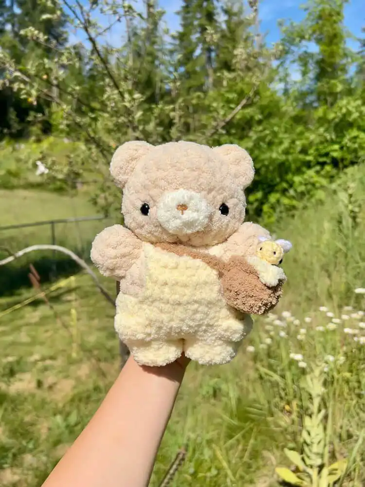 Cute crochet honey bear wearing blue overalls, smiling sweetly.