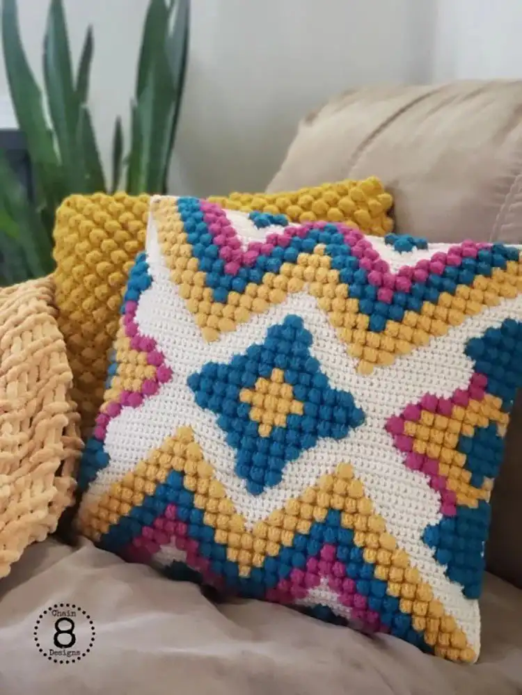 Boho-style crochet pillow with tassels, fringe, and a geometric pattern in earthy tones