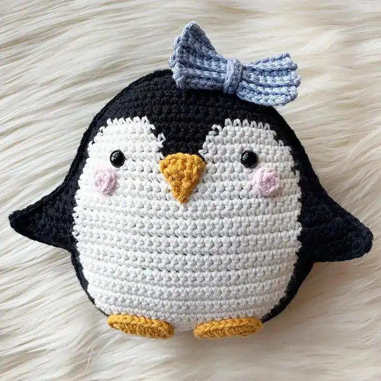 Adorable crochet penguin cushion in black and white with an orange beak and tiny bow