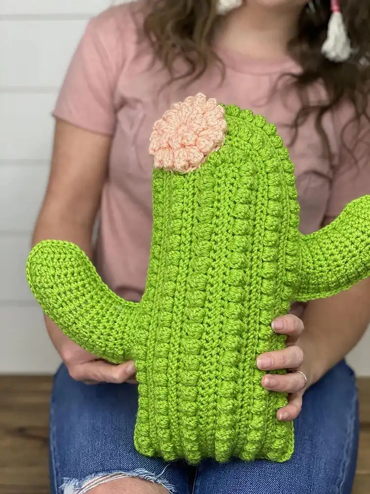 Stylish crochet cactus pillow in green with small white 'spikes' and a pink flower