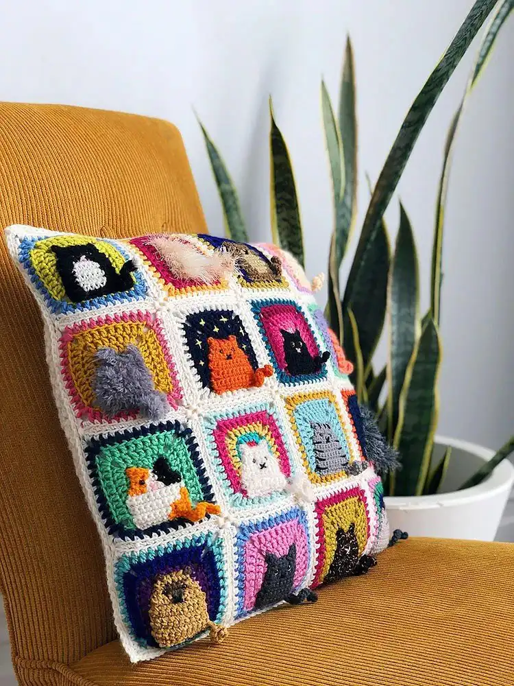 Square crochet pillow cover featuring multiple cat faces or silhouettes in different colors
