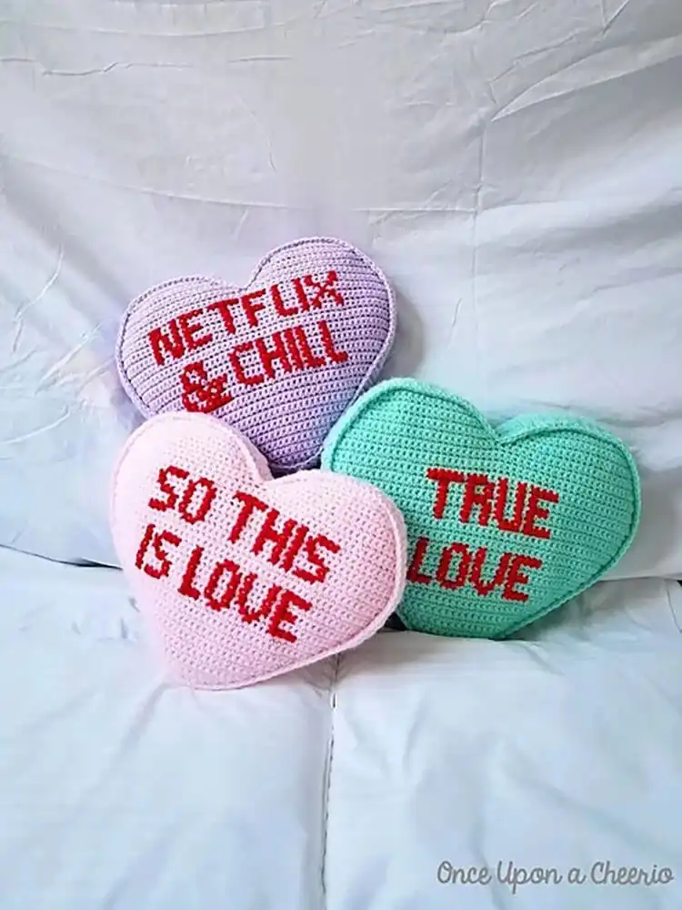 Pastel pink crochet candy heart pillow with 'HUG ME' embroidered on it