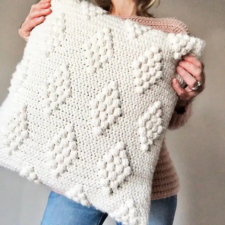 Crochet pillow featuring a diamond pattern created with raised puff stitches in a solid blue yarn
