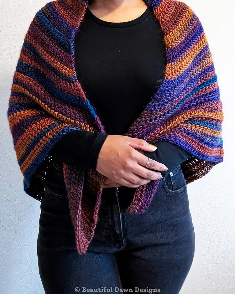 A finished Sunset Peaks Triangle Shawl in variegated yarn, featuring shades of orange, yellow, and purple, draped elegantly.