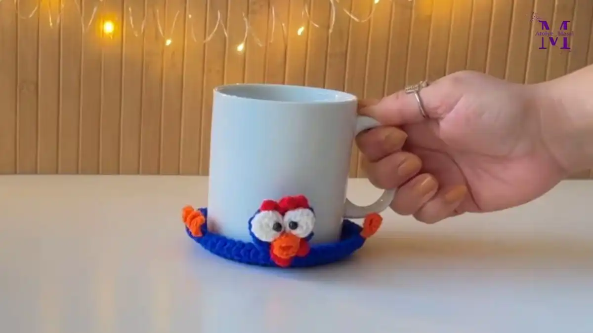 A charming, handmade Cute Crochet Chicken Mug Coaster in white and blue, hugging a coffee mug, showcasing the mug hugger pattern and its potential as an easy gift idea.