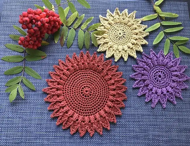A dark crocheted spider coaster with eight legs, designed for Halloween decor, displayed on a dark surface.