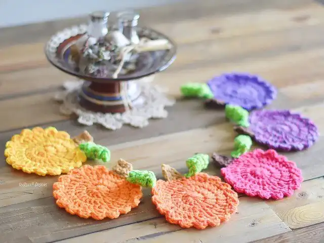 A crocheted succulent in a pot, surrounded by green doilies and various craft supplies, representing a Succulent Coaster Set.