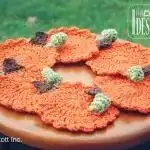 An Ellas Autumn Coaster, a crocheted sunflower doily with vibrant red and yellow petals, displayed on a blue textured surface with fall berries.