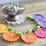 Five crochet Leaf Coasters in rich red, yellow, orange, brown, and green, arranged in a circle on a wooden table, depicting autumn foliage.