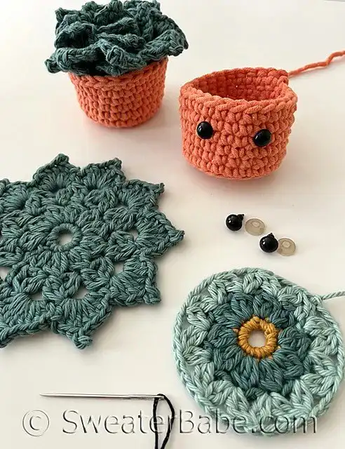 Crocheted pumpkin appliques in yellow, pink, and white yarn displayed with pinecones and craft tools, perfect for fall decoration or coasters.