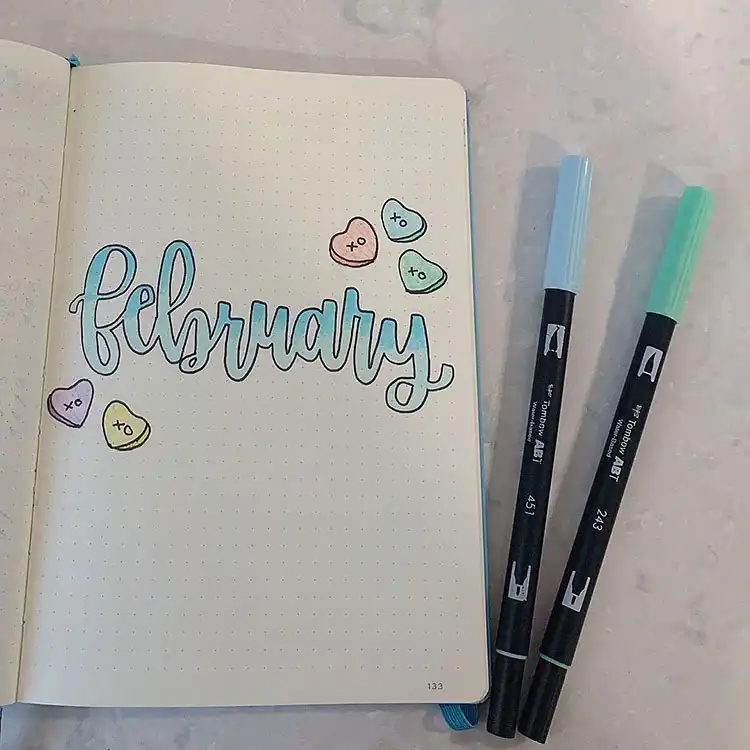 Festive February bullet journal cover page with stars, heart streamers, cupcakes, and hot drinks.