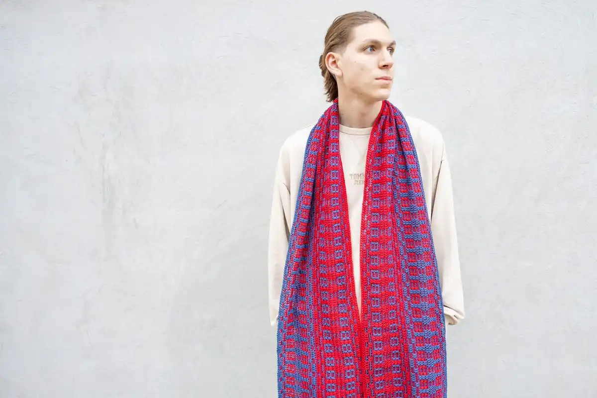 Man wearing a long mosaic crochet scarf in vibrant blue and red, showcasing the Fire and Ice Scarf Free Crochet Pattern design.