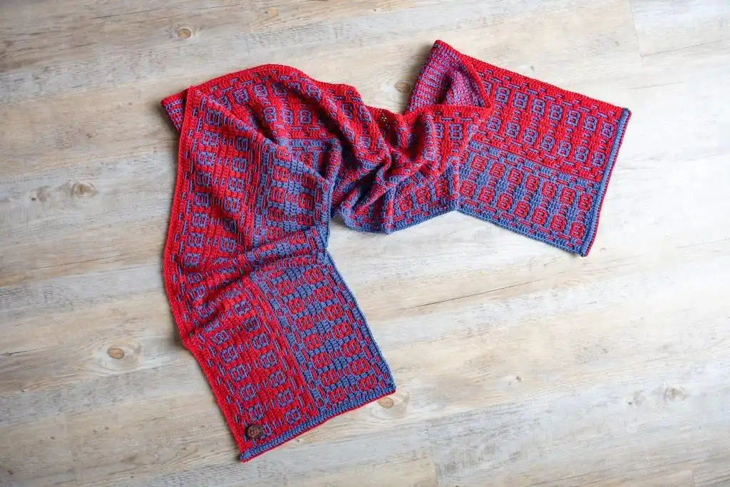 Close-up of a mosaic crochet scarf in blue and red laid on a floor, highlighting the Fire and Ice Scarf Free Crochet Pattern texture.