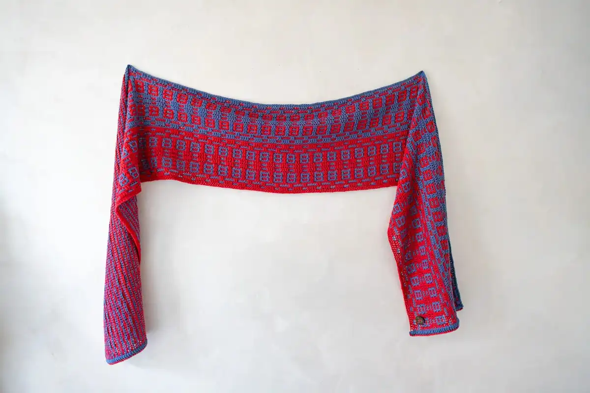 Mosaic crochet scarf in striking blue and red hanging on a wall, displaying the full length of the Fire and Ice Scarf Free Crochet Pattern.