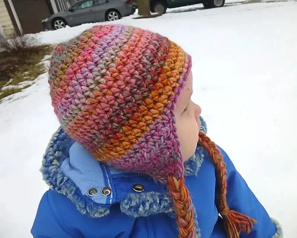A baby wearing an adorable crocheted aviator hat inside a cardboard box, showcasing the Crochet Aviator Hat from Free Crochet Hat Patterns for Babies and Kids.