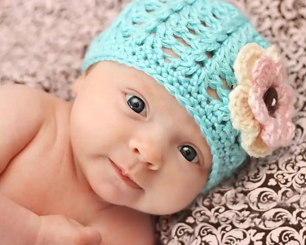 A little girl wearing a knit hat with flower details while holding a lollipop, showcasing the Perenni pattern from Free Crochet Hat Patterns for Babies and Kids.