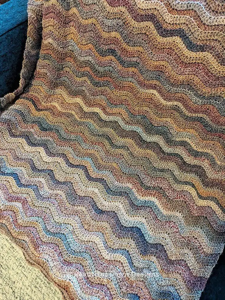 Close-up of the finished Free Crochet Pattern for a Ripple Stitch Blanket Fun and Beginner Friendly on a couch, highlighting the yarn texture.