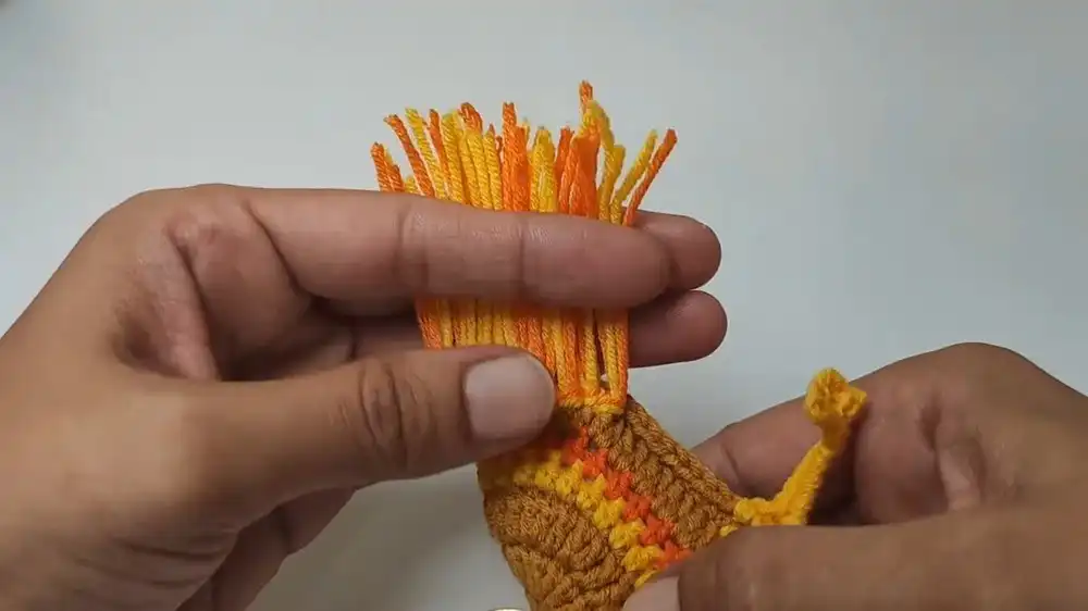 Colorful tassels being attached to form the fluffy tail of the Free Crochet Rooster Keychain Pattern.