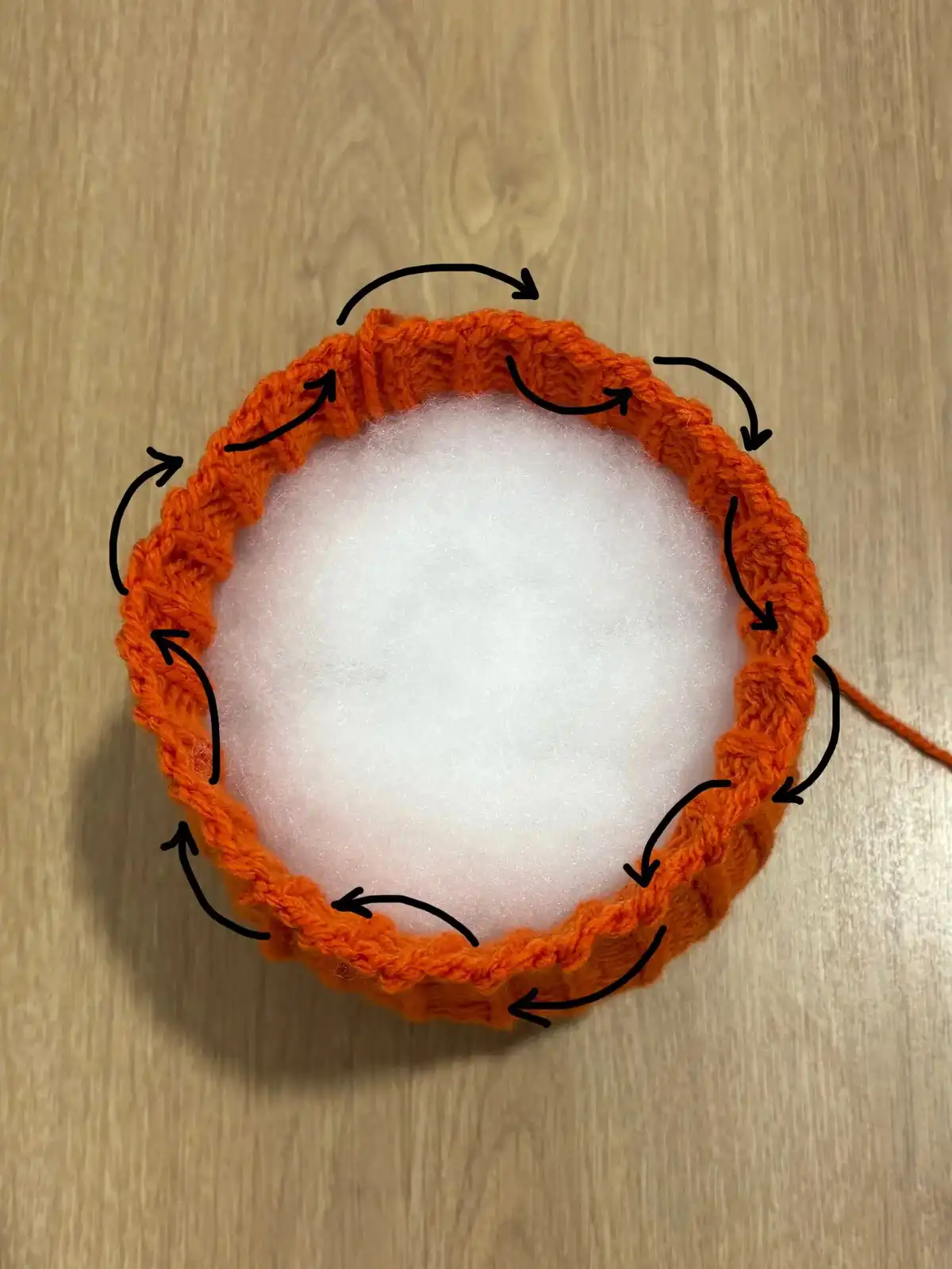 A hand holding a yellow ribbed 'No Slip Stitch Given Pumpkin' with a striped grey and white leaf and curly brown stem, designed by Ana-Maria.