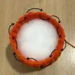 A stack of three chunky fall pumpkins crocheted in cream, orange, and gray yarn, designed by Heather J Anderson, arranged on a small wooden tray.