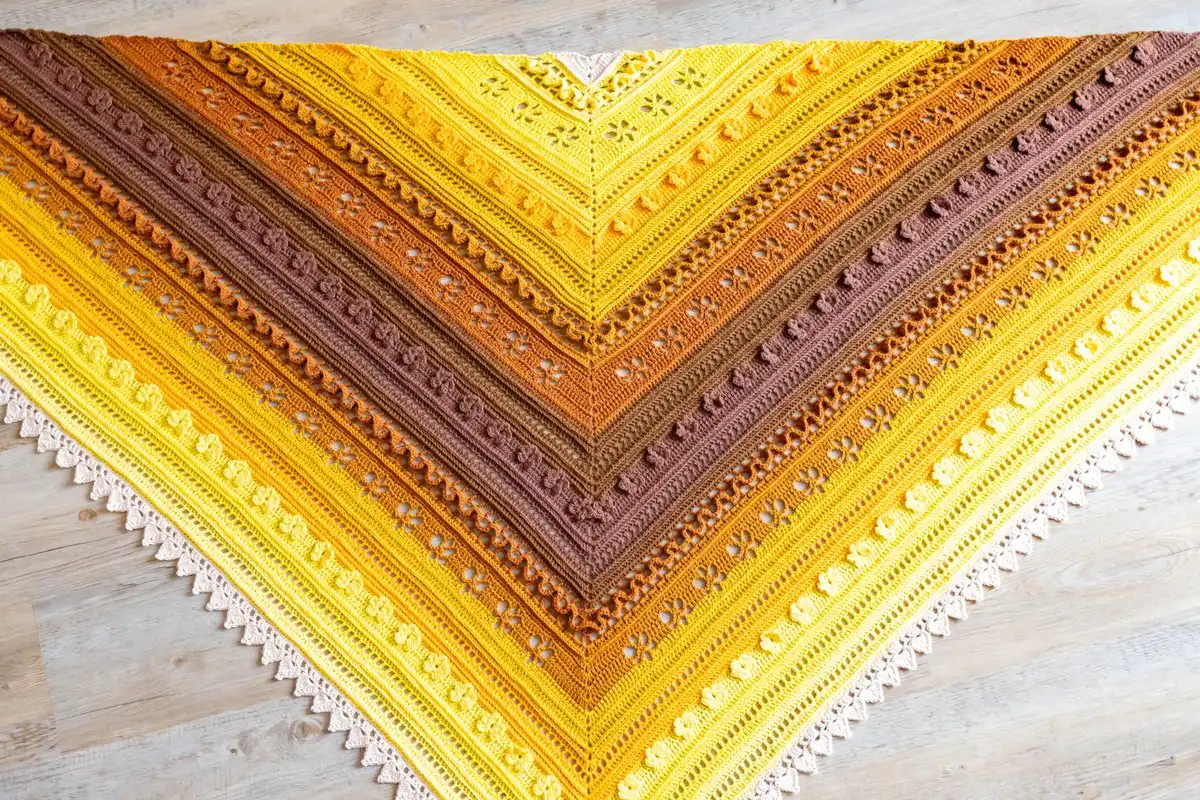 Close-up of the Golden Harvest Shawl's delicate lace motifs and textured stitches, highlighting the autumnal yarn colors.
