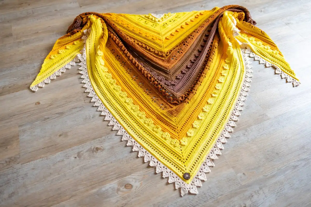 Crochet triangle shawl in brown and golden yellow hues, spread out to display its large size and flowing drape.