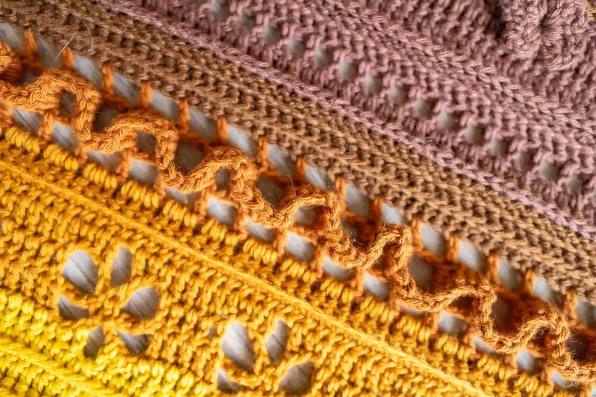 Detailed view of a crocheted triangle shawl, focusing on the golden yellow and brown color combination and textured stitches.