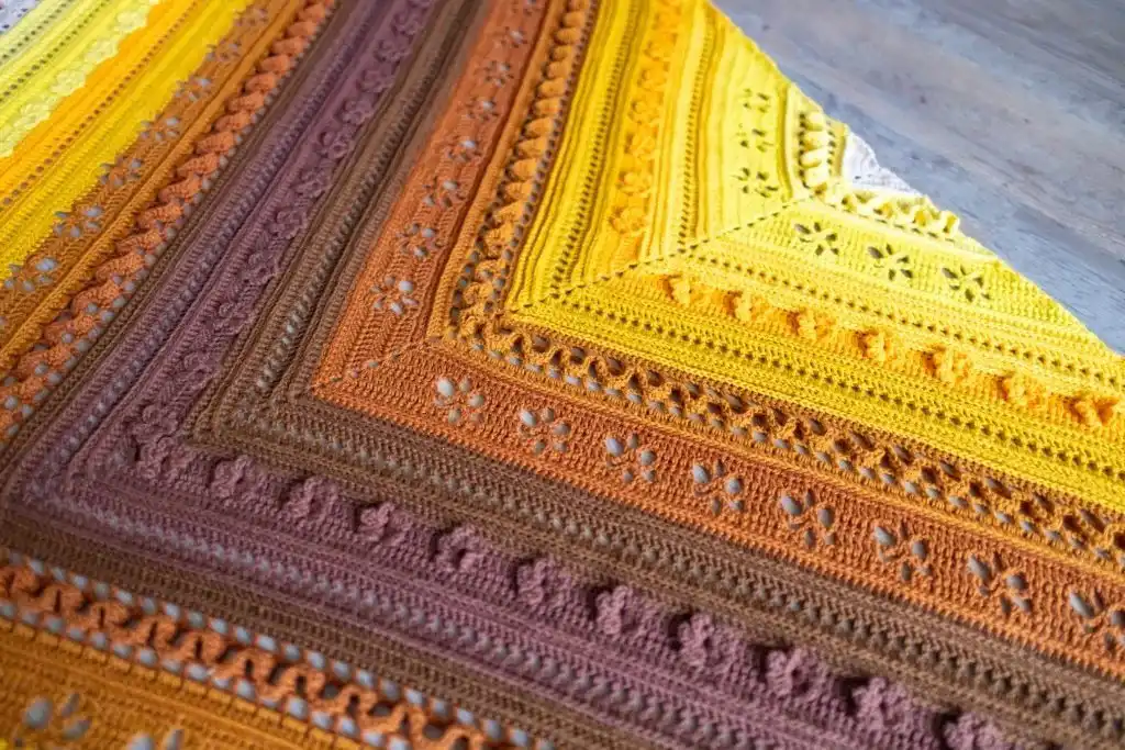 Detailed image of the filet crochet flowers in brown color within the Golden Harvest Shawl pattern, showcasing the intricate floral design.