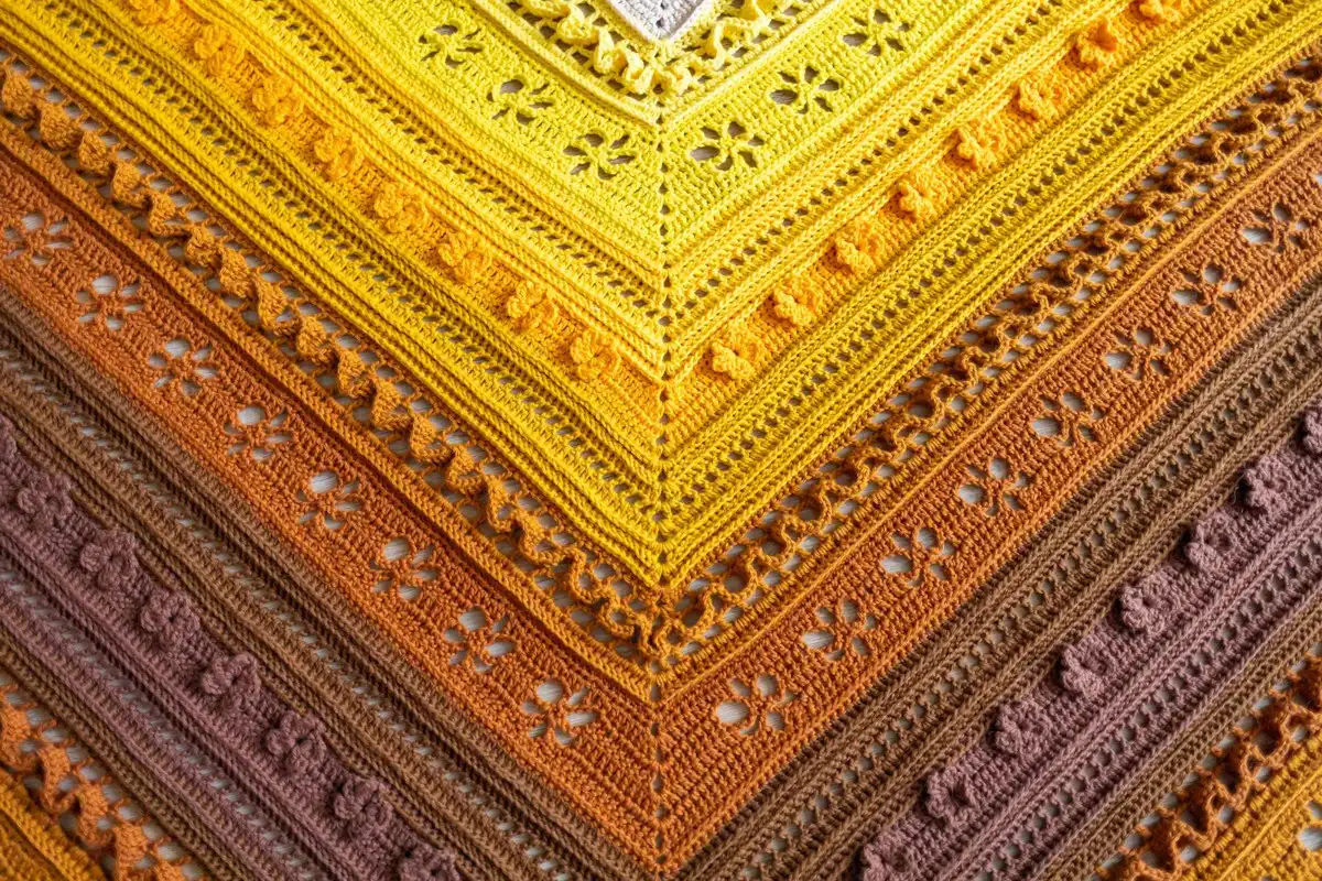 Overhead shot of the crochet triangle shawl in various shades of brown and yellow, highlighting a transitional 'Bridge' section.