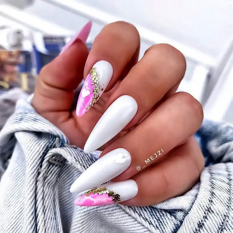 Stiletto nails featuring a pink and white marble pattern, elegant gold foil, and romantic heart embellishments.