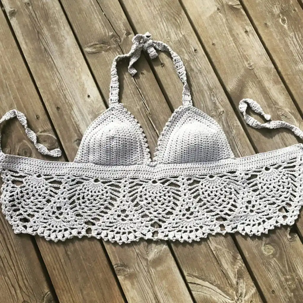 White crochet crop top with a central lace design, laid flat on denim jeans on a wooden surface.