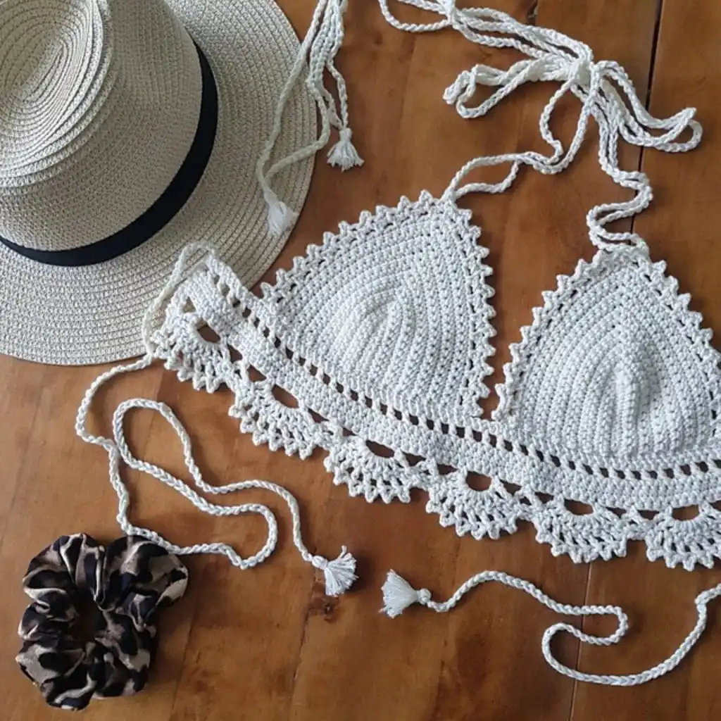 Intricate crochet crop top with lace patterns and delicate tie-up straps, resting on a wooden surface.