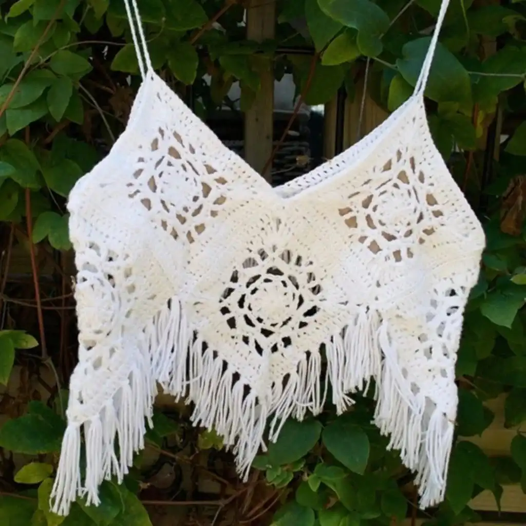 Person wearing a stylish white crochet crop top and blue jeans against a plain background.