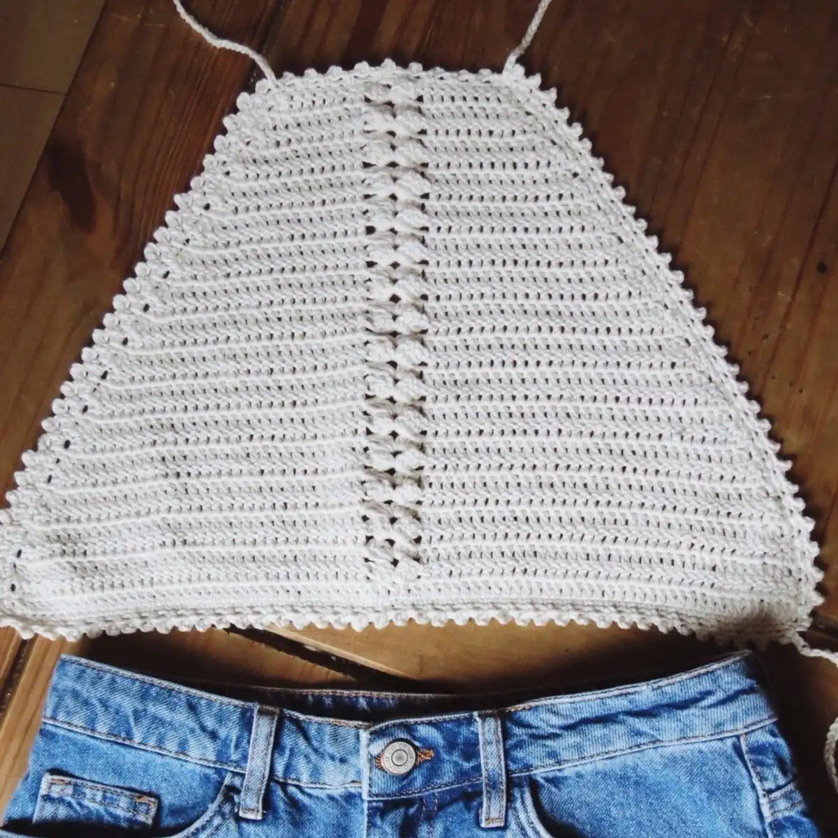 Person elegantly wearing a crochet halter crop top with a scalloped edge and a pendant necklace.