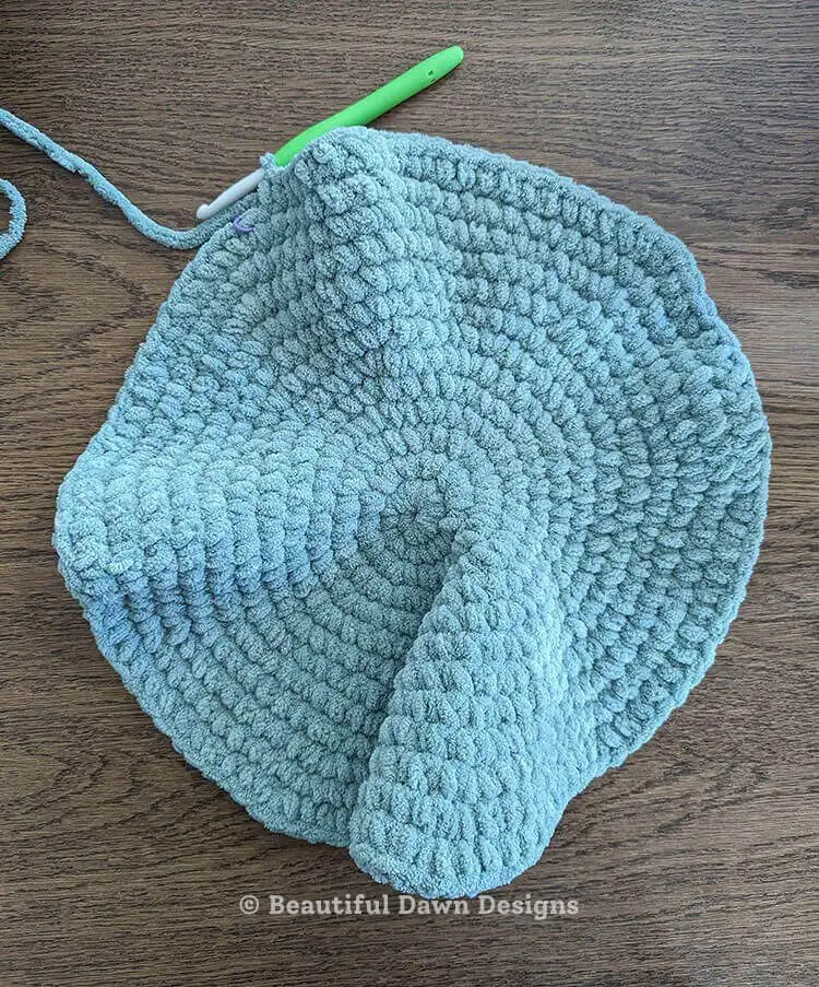 Hands demonstrating how to fold the large crocheted circle in half, aligning stitches for the moon pillow's shape. Moon Pillow Crochet Pattern assembly.