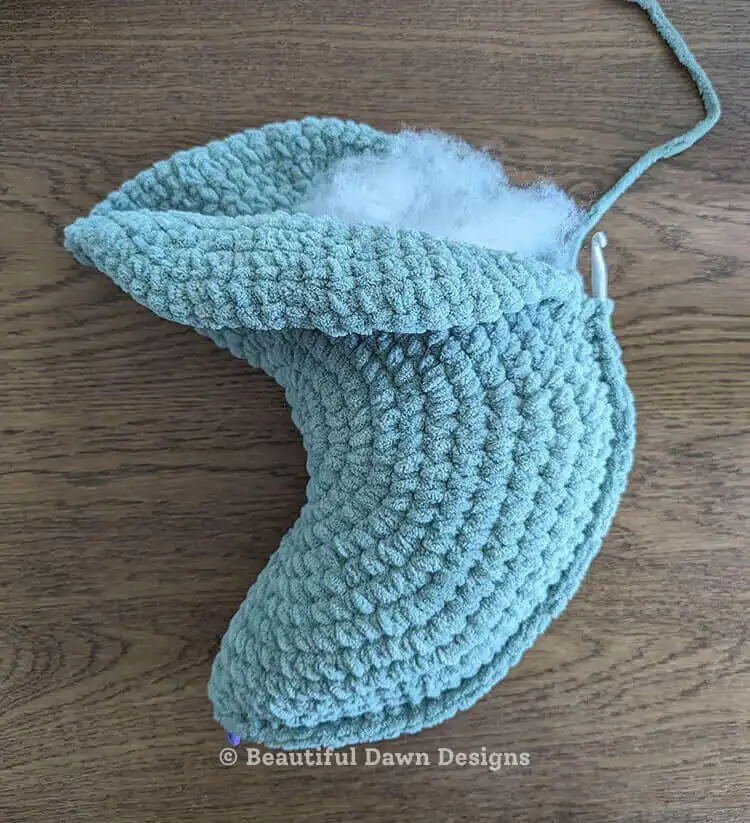 A finished blue crescent moon pillow with a subtle textured surface, showcasing an alternative color option for the free crochet pattern. Moon Pillow Crochet Pattern display.