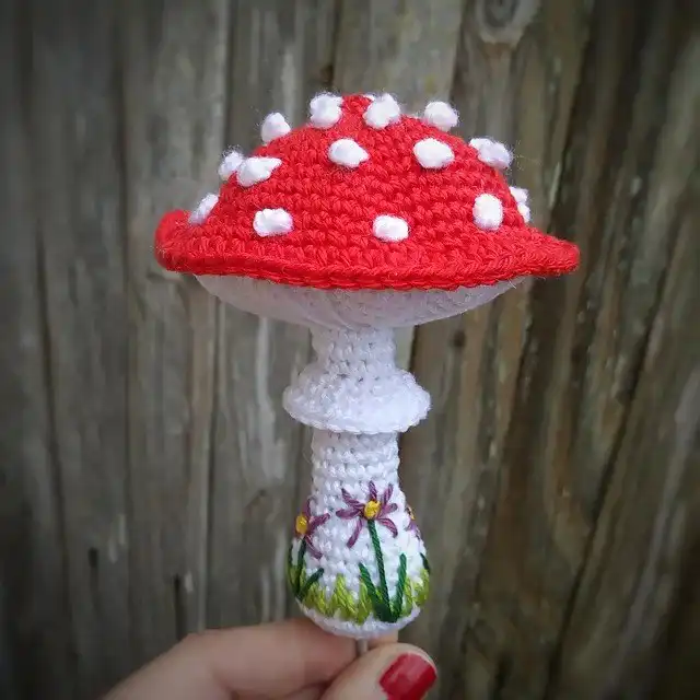 A classic red and white polka-dotted toadstool amigurumi, featuring a small door, resembling a fairy house, from the free patterns.