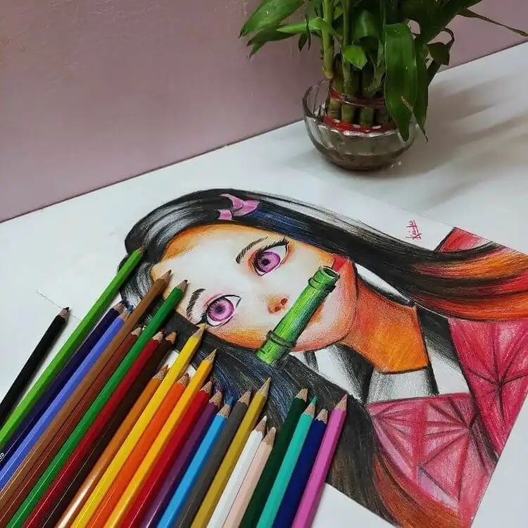 Artist's hand coloring a Nezuko drawing with colored pencils, demonstrating reference use
