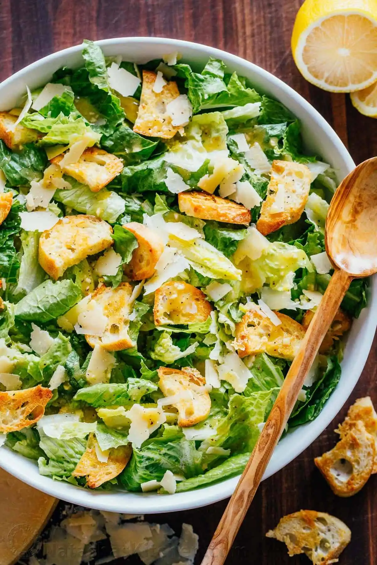 A beautifully arranged classic Caesar Salad in a wooden bowl with crisp romaine, golden croutons, and shaved Parmesan.