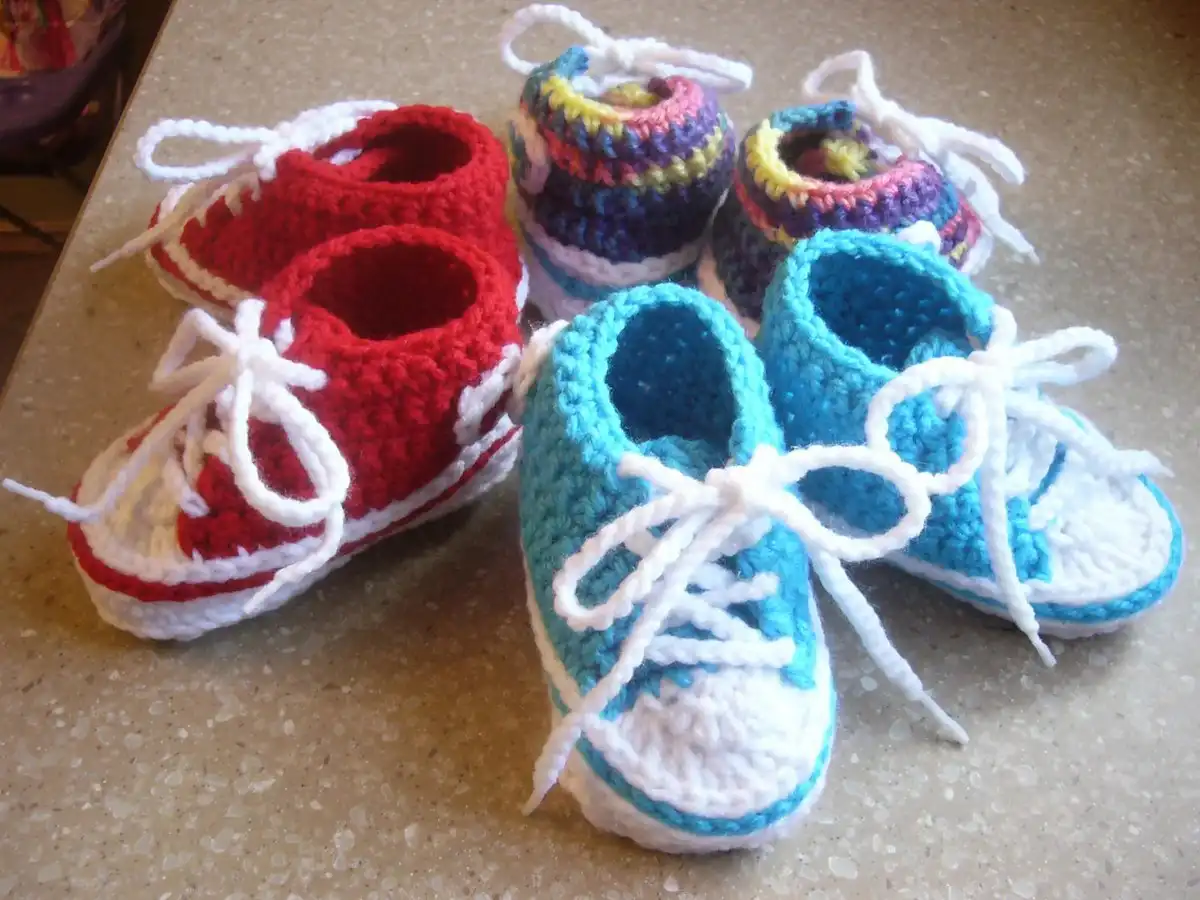 Three pairs of crocheted Baby Converse booties in red, blue, and multicolor, styled like sneakers with white laces.