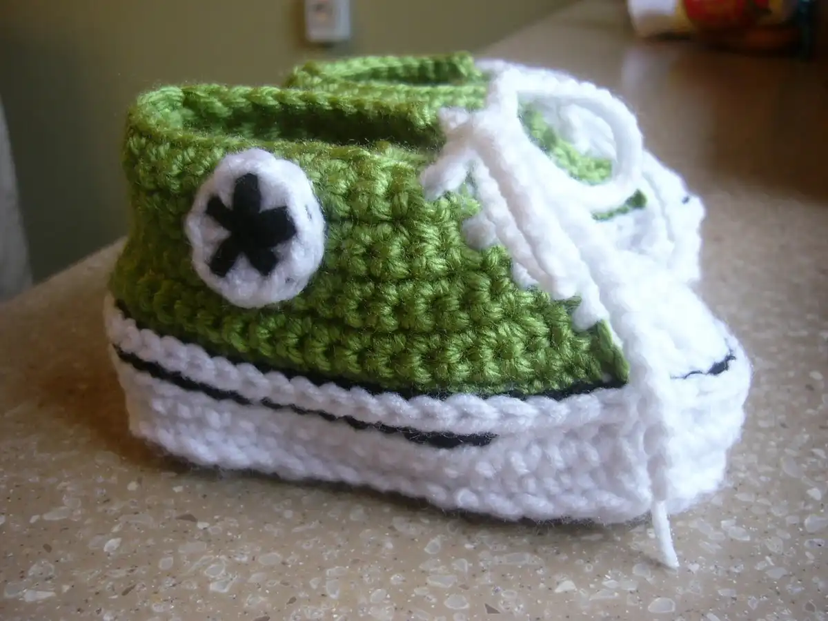 Vibrant crocheted baby booties resembling Converse sneakers with laces, ready for a video tutorial.