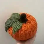 Three small rustic crocheted pumpkins in brown, yellow, and white, each featuring a cinnamon stick stem, arranged on a wooden surface.