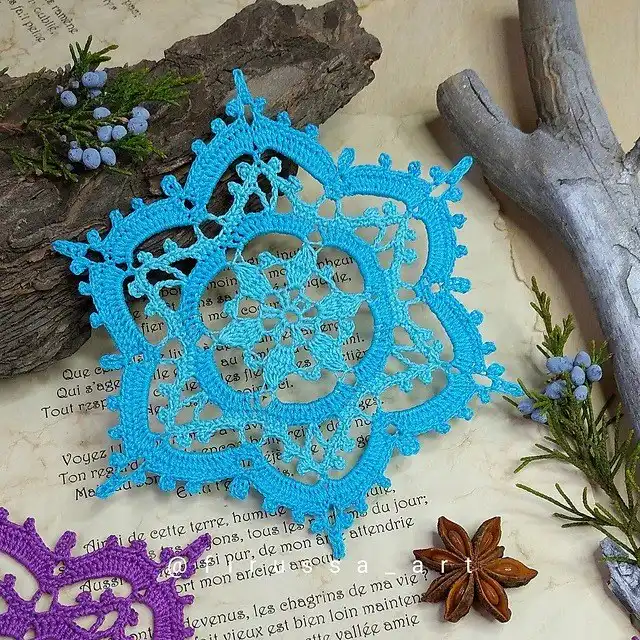 A sparkling 'Helina Snowflake' crochet ornament, made with glittery yarn, perfect for a festive Christmas tree decoration.