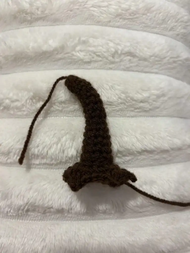 A small, brown, crocheted object shaped like a wizard hat, representing the fully formed stem with stuffing and bend.