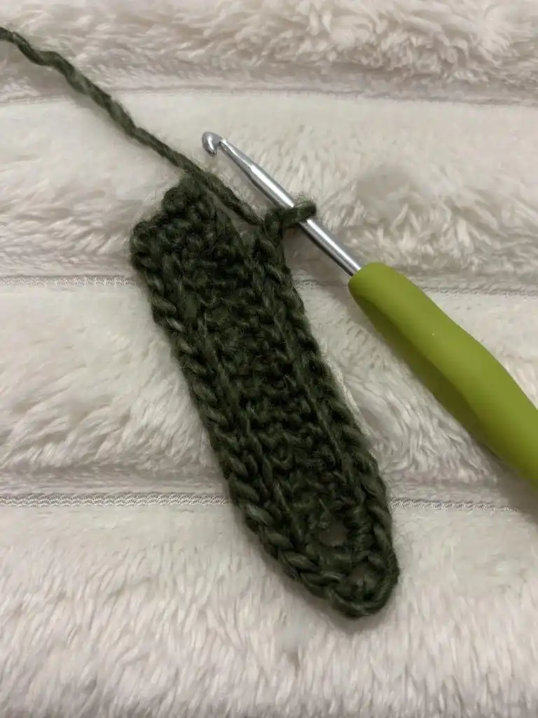 A green crochet leaf in progress, displaying the developing shape and texture of the leaf design.