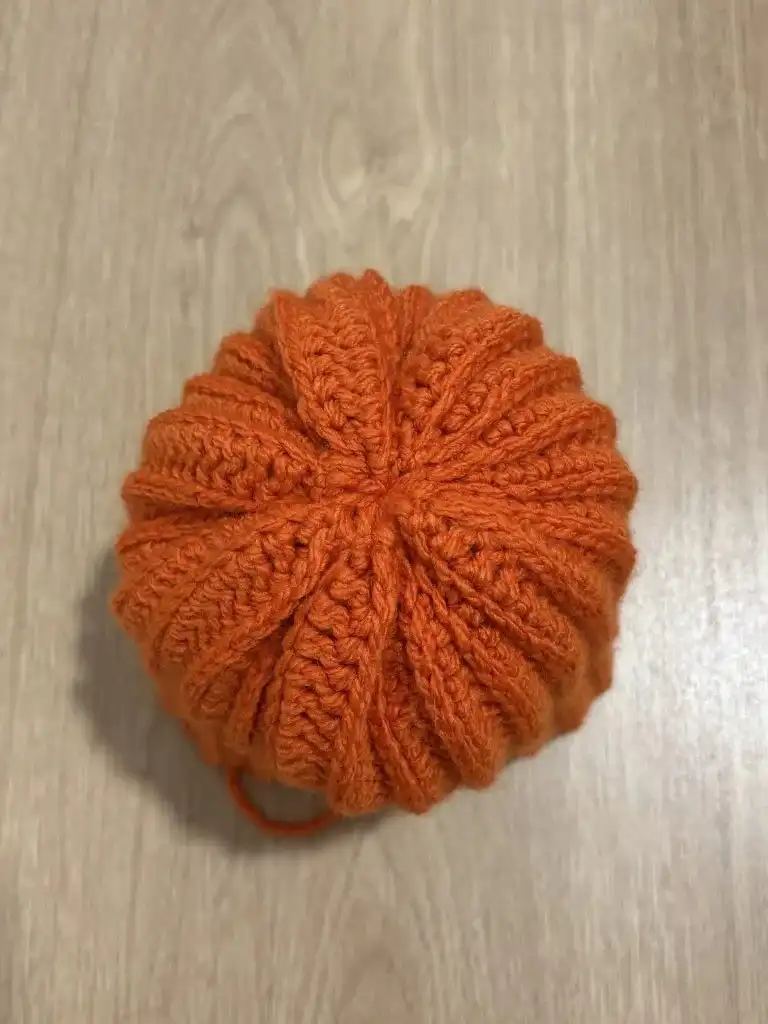 Yarn being pulled through the top stripes of the pumpkin to close it, mirroring the bottom cinching.