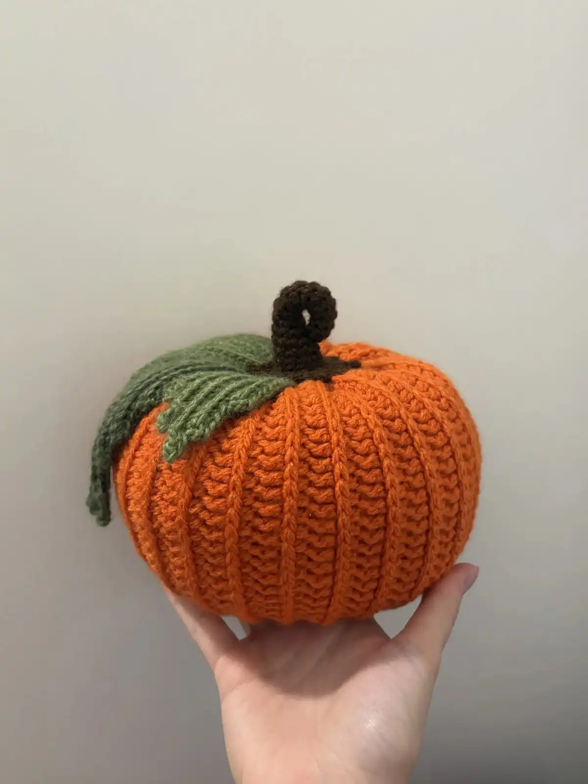 A hand holding an in-progress crochet pumpkin, illustrating the texture created by the stitches mentioned in the Pumpkin Free Crochet Pattern.