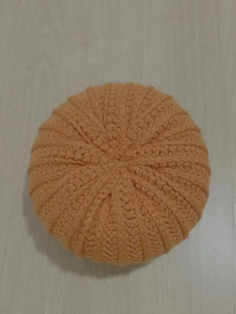 Sewing the edge of the crochet leaf onto the pumpkin, showing the process of secure attachment.