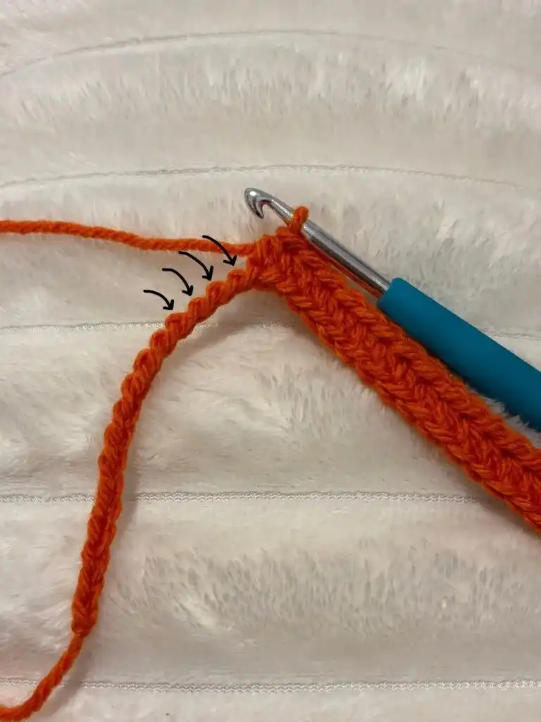 A crochet hook working into an orange crocheted fabric, showing the third loop only technique for the pumpkin panel.