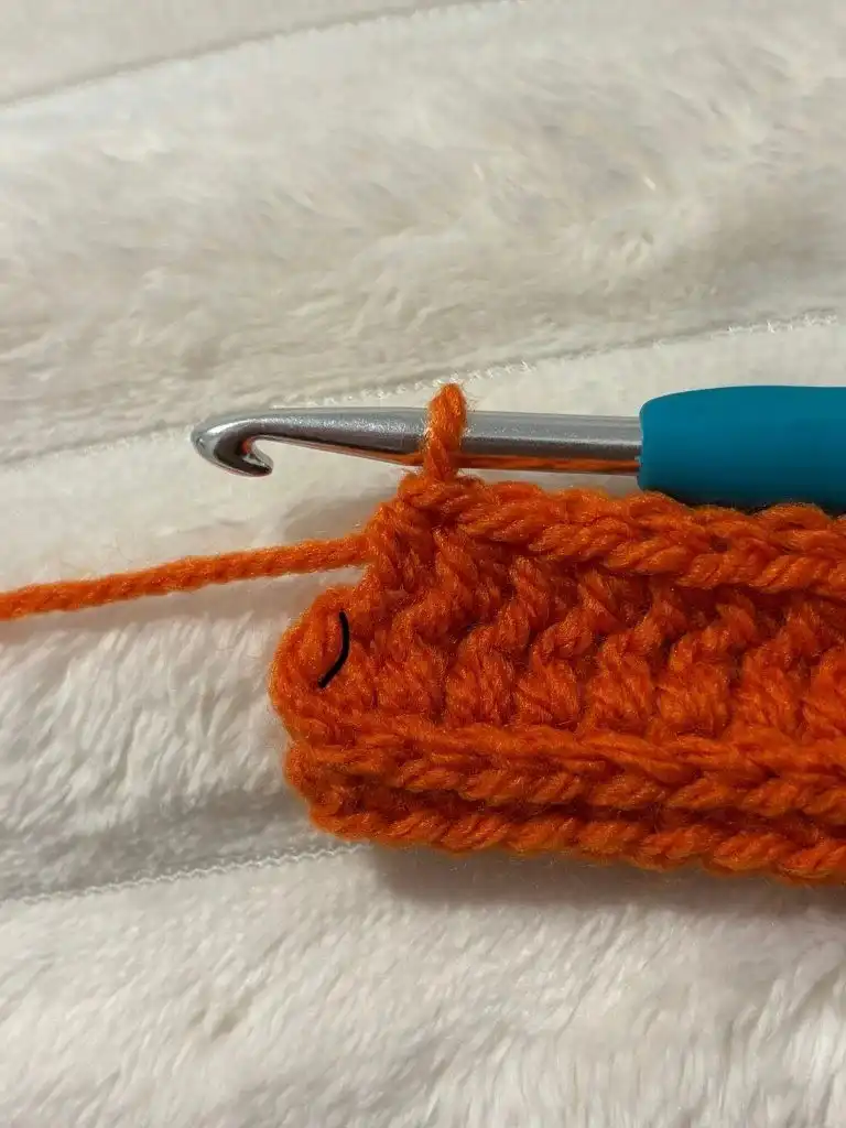 A rectangular piece of orange crocheted fabric with horizontal ridges, representing the completed pumpkin panel before assembly.